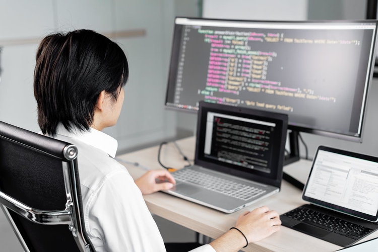 Um analista de BI trabalhando em seu computador com múltiplas telas, exibindo código SQL para a extração de dados.
